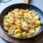 two plates filled with potato egg scramble on top of a wooden table next to an orange napkin