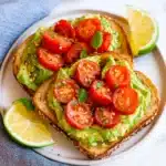 two pieces of toast with avocado and tomatoes on it sitting on a plate