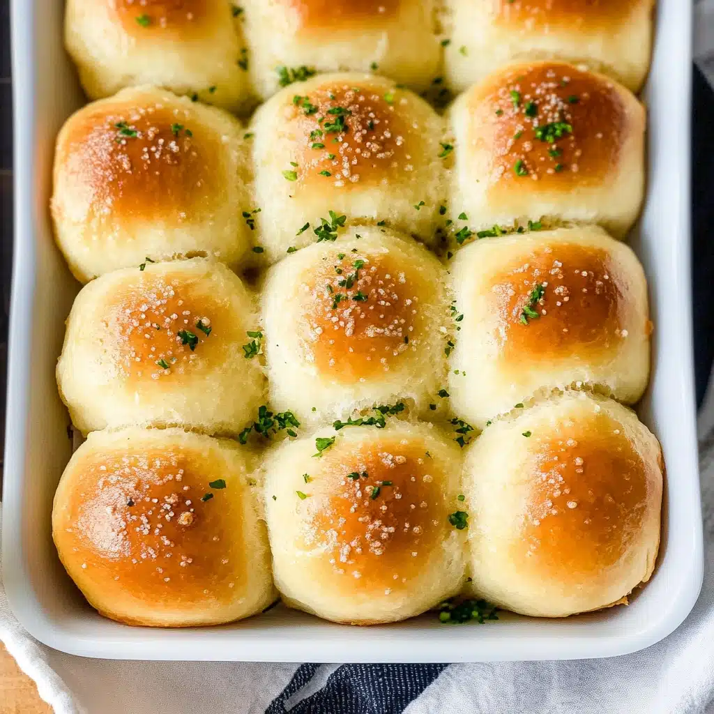 a hand holding a piece of garlic parmesan dinner rolls over a baking pan