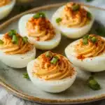 a white bowl filled with deviled eggs topped with sesame seeds and garnishes