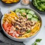 healthy loaded cheeseburger bowls in a bowl with french fries and pickles on the side