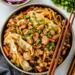 two bowls filled with noodles and topped with sauce, green onions, carrots and shredded meat