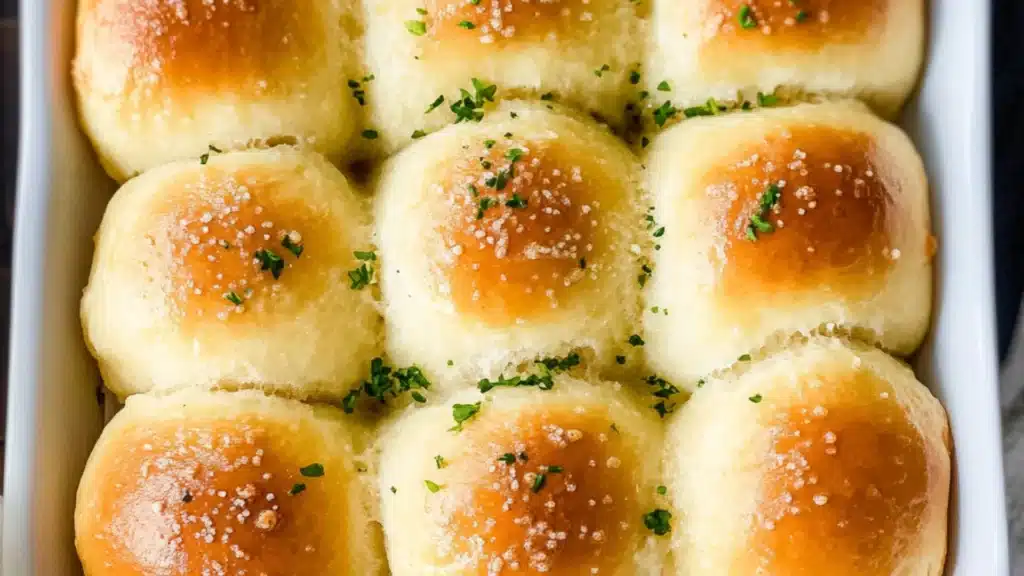a hand holding a piece of garlic parmesan dinner rolls over a baking pan
