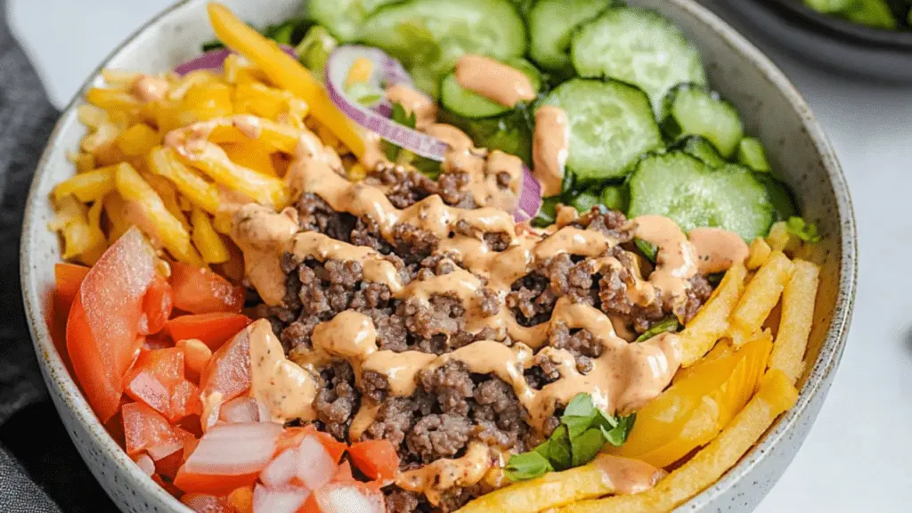 healthy loaded cheeseburger bowls in a bowl with french fries and pickles on the side