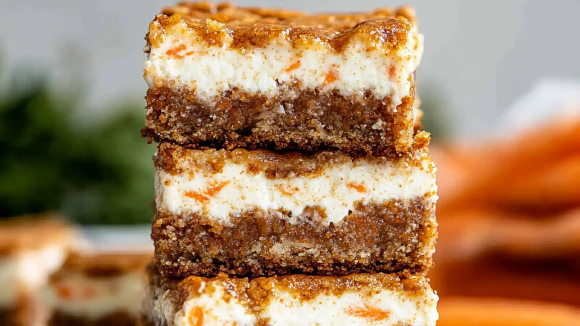 carrot cake cheesecake bars on a cooling rack with carrots and other dessert items