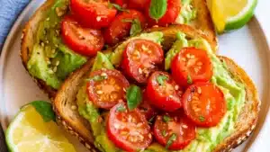two pieces of toast with avocado and tomatoes on it sitting on a plate