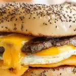 steak egg and cheese bagel sandwich on a wooden cutting board with text overlay that reads steak egg and cheese bagel sandwich