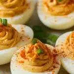 a white bowl filled with deviled eggs topped with sesame seeds and garnishes