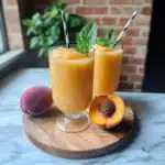two glasses filled with frozen peach lemonade slushies