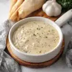 creamy garlic parmesan sauce on a spoon in a casserole dish with text overlay