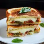 the sun dried tomato bacon pesto grilled cheese sandwich is cut in half and stacked on top of each other