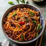 a bowl filled with noodles and meat on top of a white tablecloth next to chopsticks