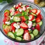two bowls filled with strawberries and cucumber salad next to lemon wedges