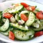 a white plate topped with cucumber salad and text that reads mom's classic tomato and cucumber salad