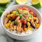 southwest chicken bowl with rice and vegetables on the side, in a white bowl topped with dressing