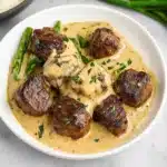 a white plate topped with meat covered in gravy and garnished with parsley
