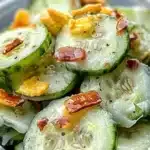 a plastic container filled with cucumber and bacon salad on top of a wooden table